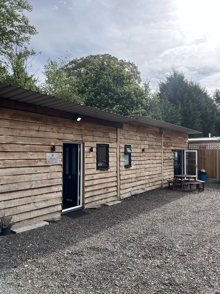 The studio from outside, a single storey wooden cabin with parking on the gravel in front
